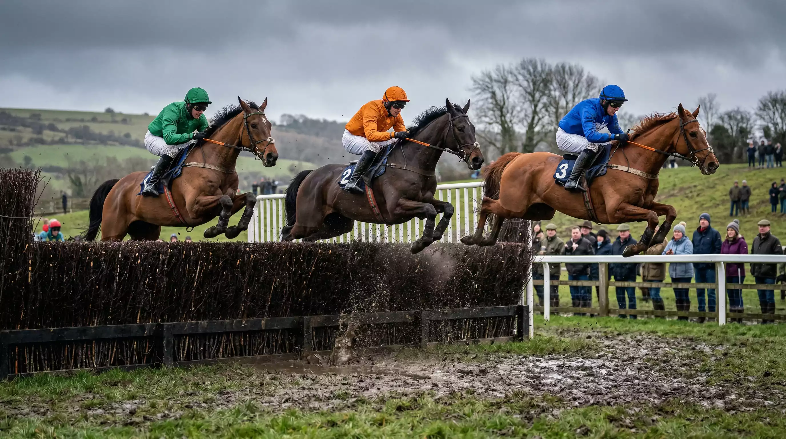 Horses clearing a fence during a National Hunt steeplechase at a British racecourse on soft ground